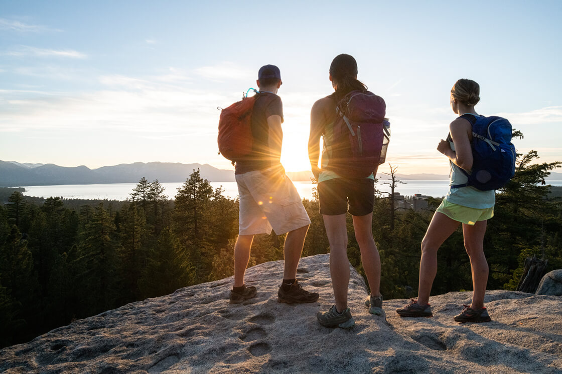 Three hikers watching the sunset from a rock